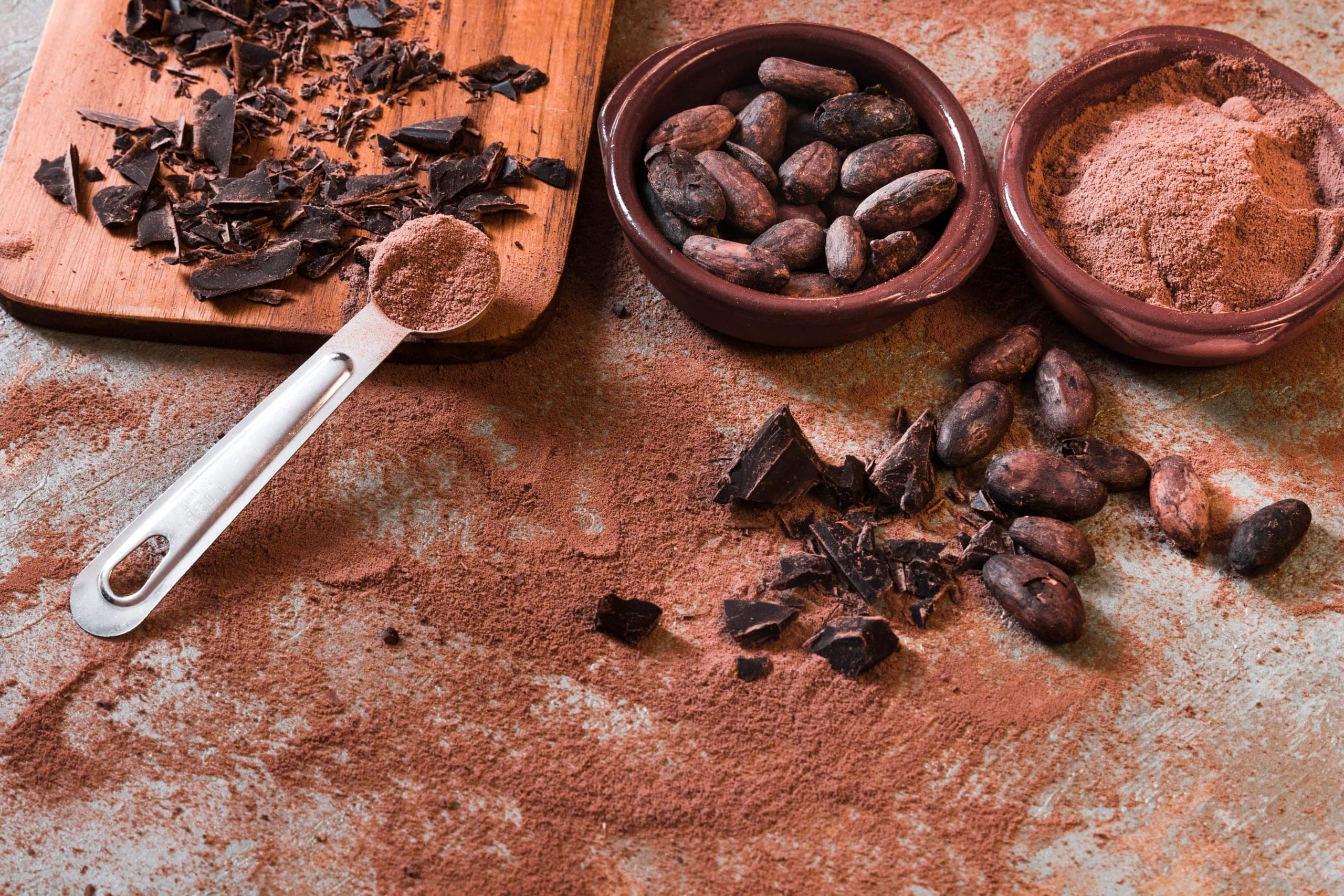 Cocoa beans, cocoa powder and broken chocolate arranged on a stone surface